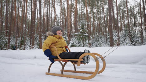 happy-child-boy-is-sitting-in-wooden-sledge-and-riding-over-snow-in-winter-forest-family-time